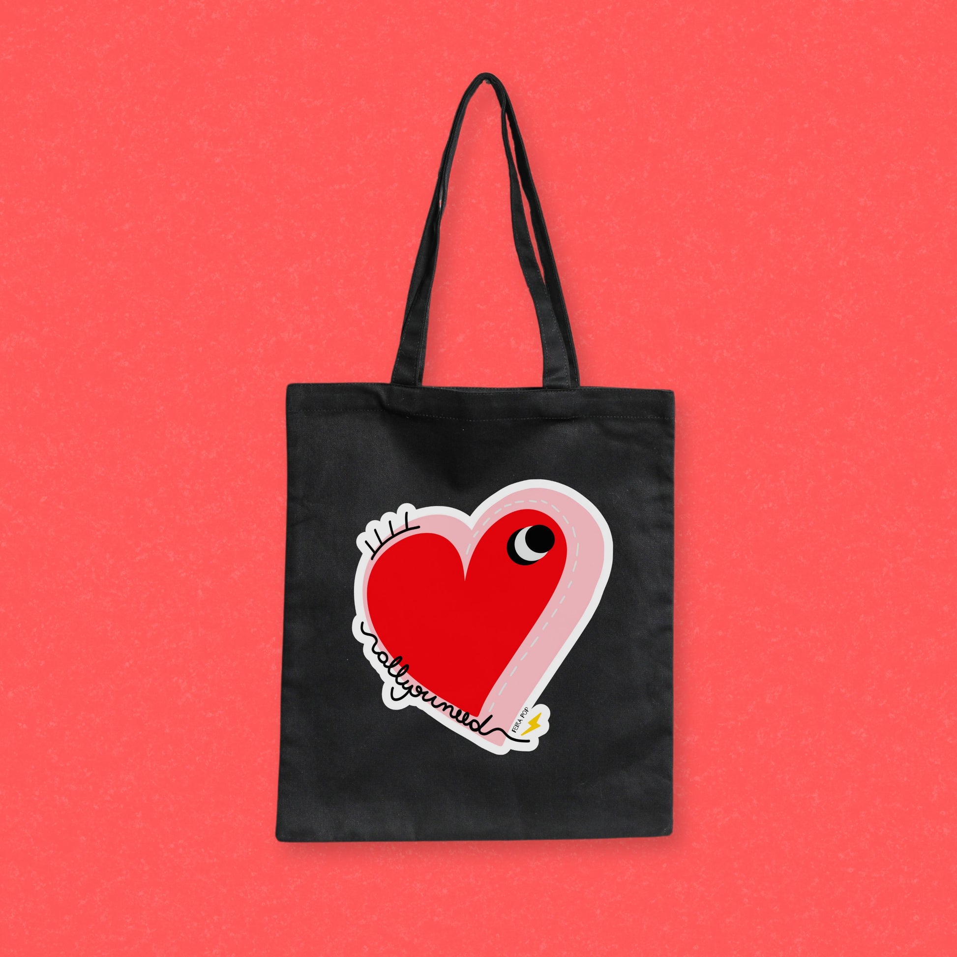 All You Need Tote Bag with original drawing of a big red heart with one eye and the words All You Need in playful font, perfect for carrying daily essentials and adding a touch of fun to any outfit.
