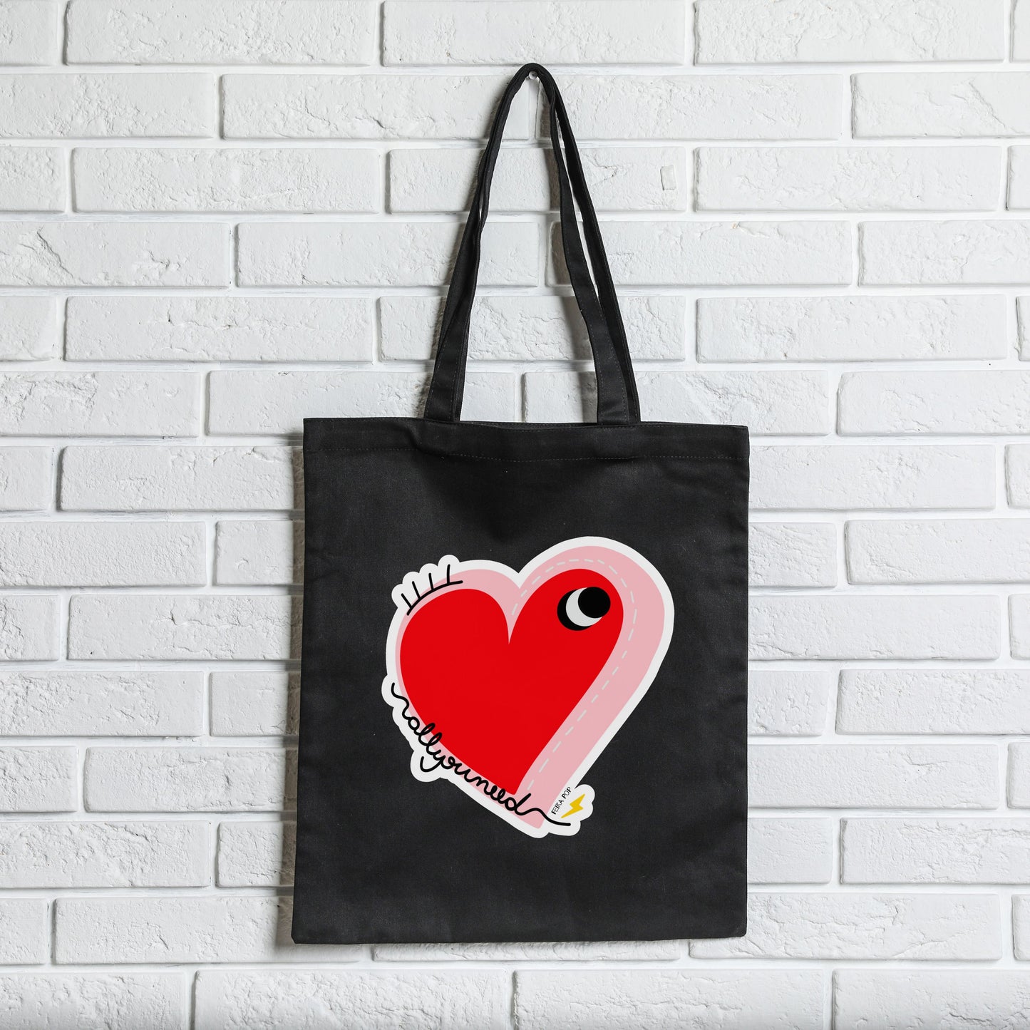 All You Need Tote Bag with original drawing of a big red heart with one eye and the words All You Need in playful font, perfect for carrying daily essentials and adding a touch of fun to any outfit.