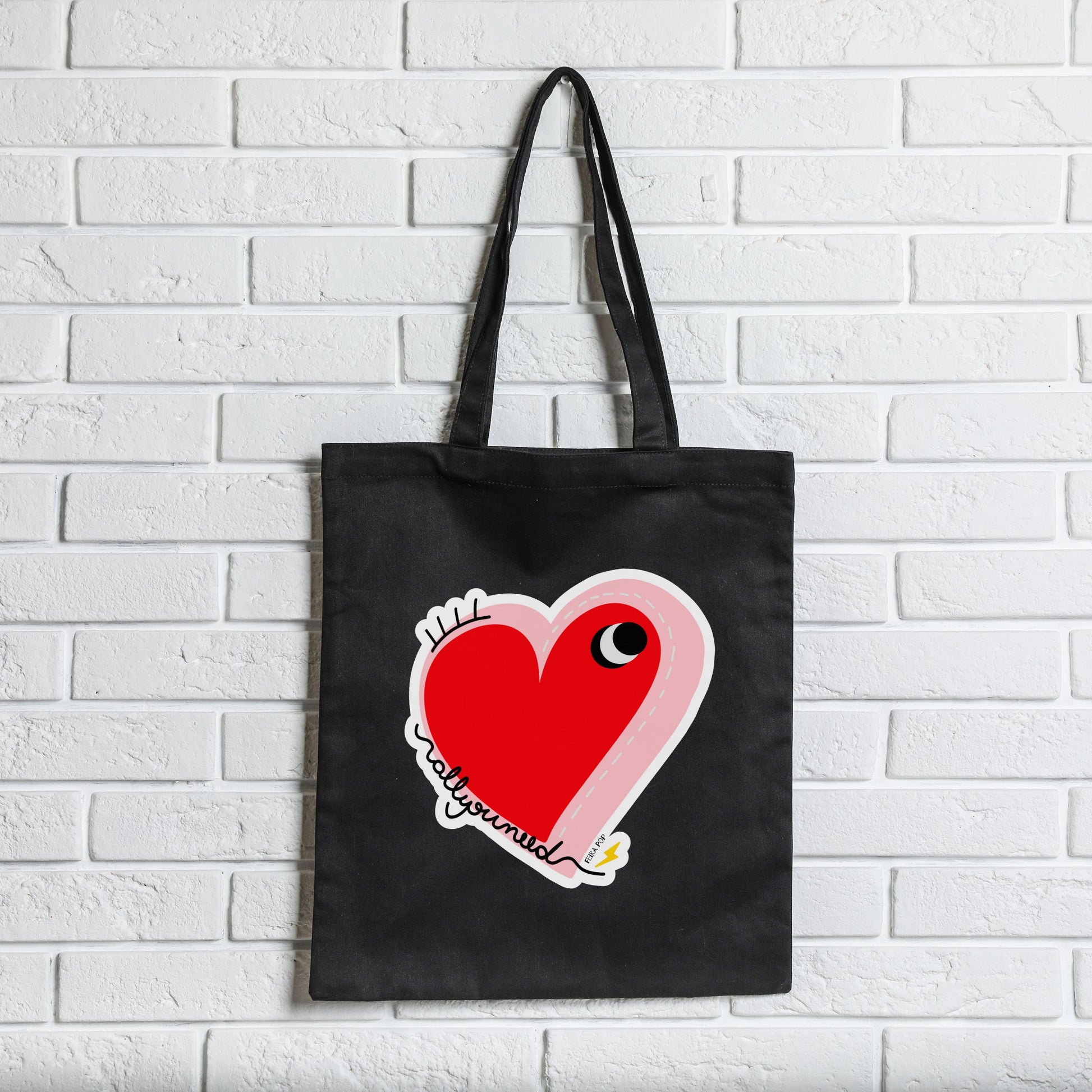 All You Need Tote Bag with original drawing of a big red heart with one eye and the words All You Need in playful font, perfect for carrying daily essentials and adding a touch of fun to any outfit.