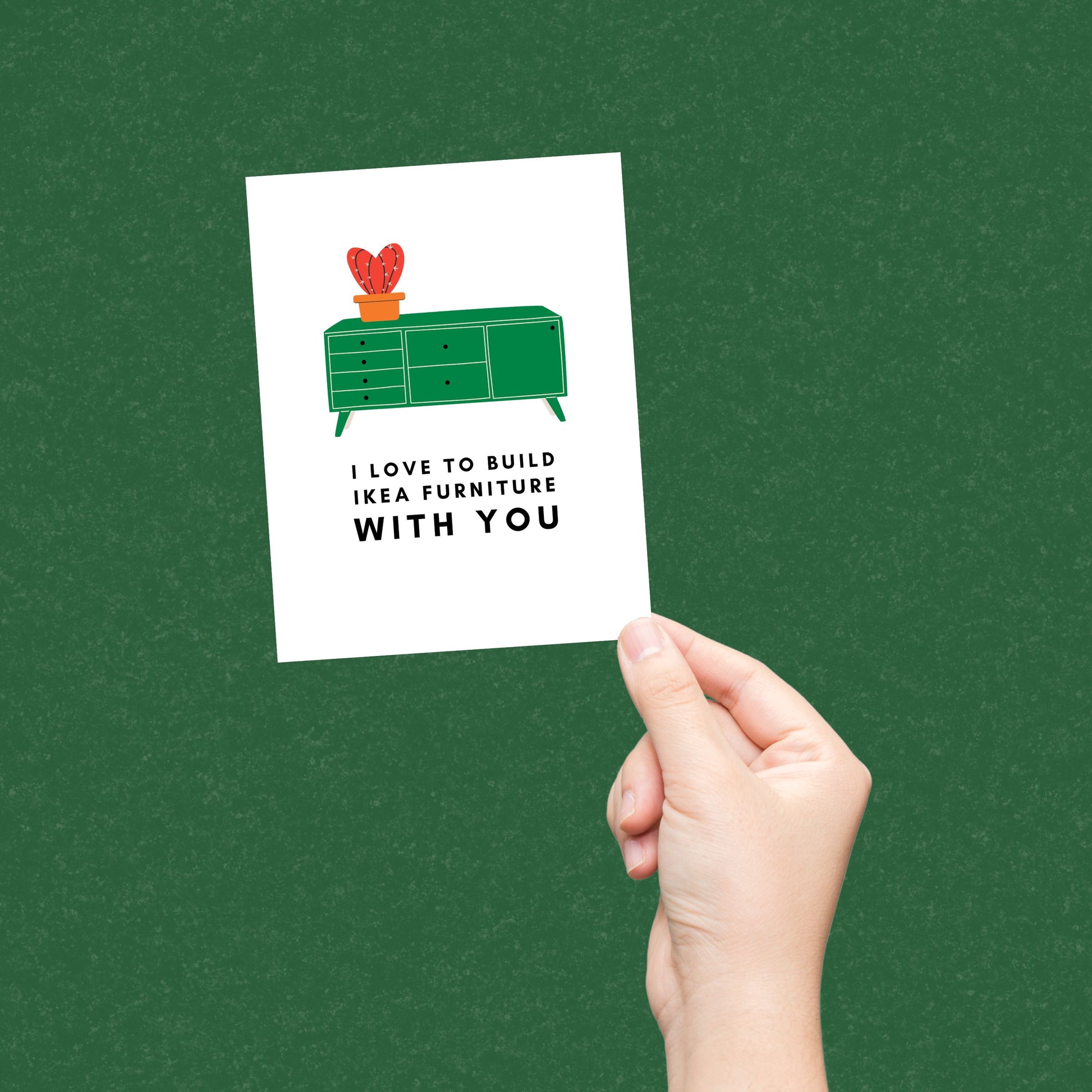 Greeting card with the phrase I Love to Build IKEA Furniture With You featuring a drawing of a green TV stand with a vase holding a red cactus on top. Perfect for celebrating relationships with humor and a nod to DIY adventures.