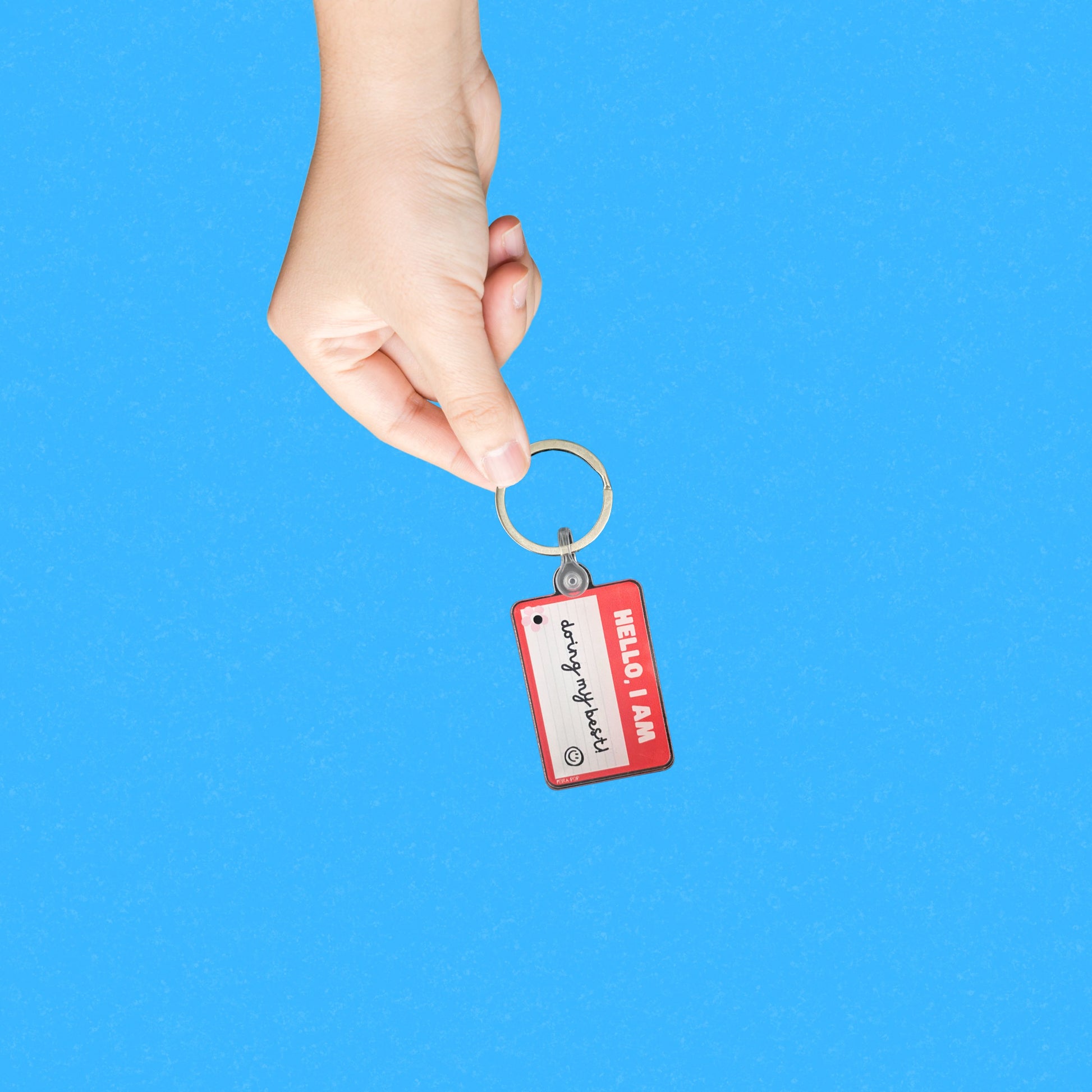 Red name tag keychain with the phrase Hello, I Am Doing My Best, humorous motivational accessory, perfect for daily encouragement and resilience, ideal gift for friends and family.