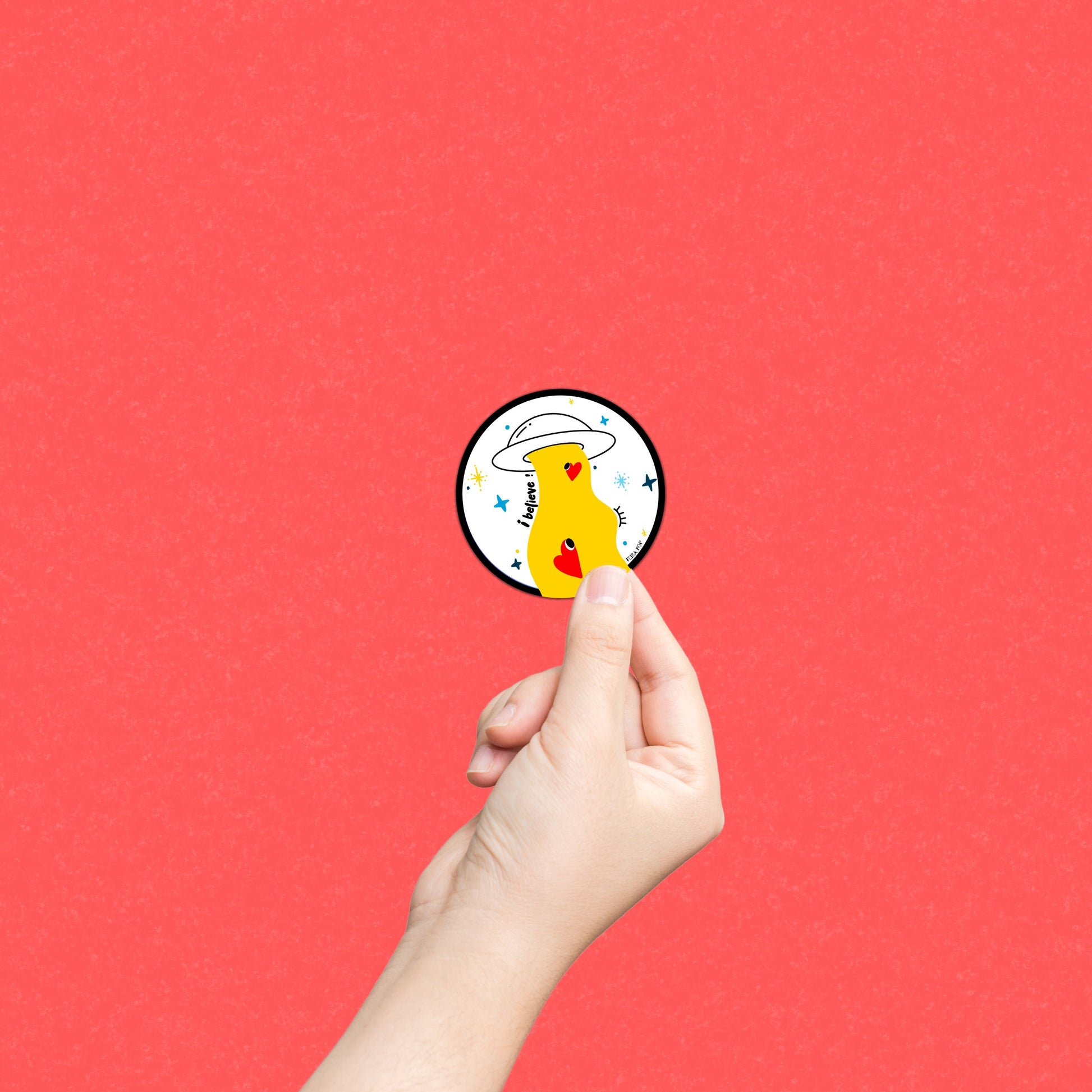 Sticker with the phrase I Believe featuring an original drawing of a UFO abducting two cute red hearts. Perfect for UFO enthusiasts and lovers of whimsical, romantic art.