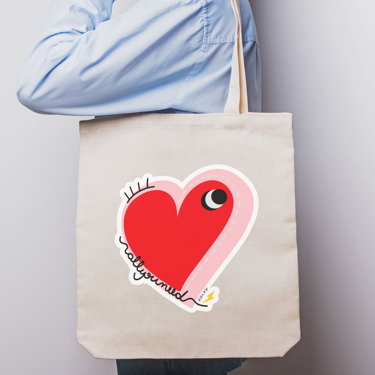 All You Need Tote Bag with original drawing of a big red heart with one eye and the words All You Need in playful font, perfect for carrying daily essentials and adding a touch of fun to any outfit.