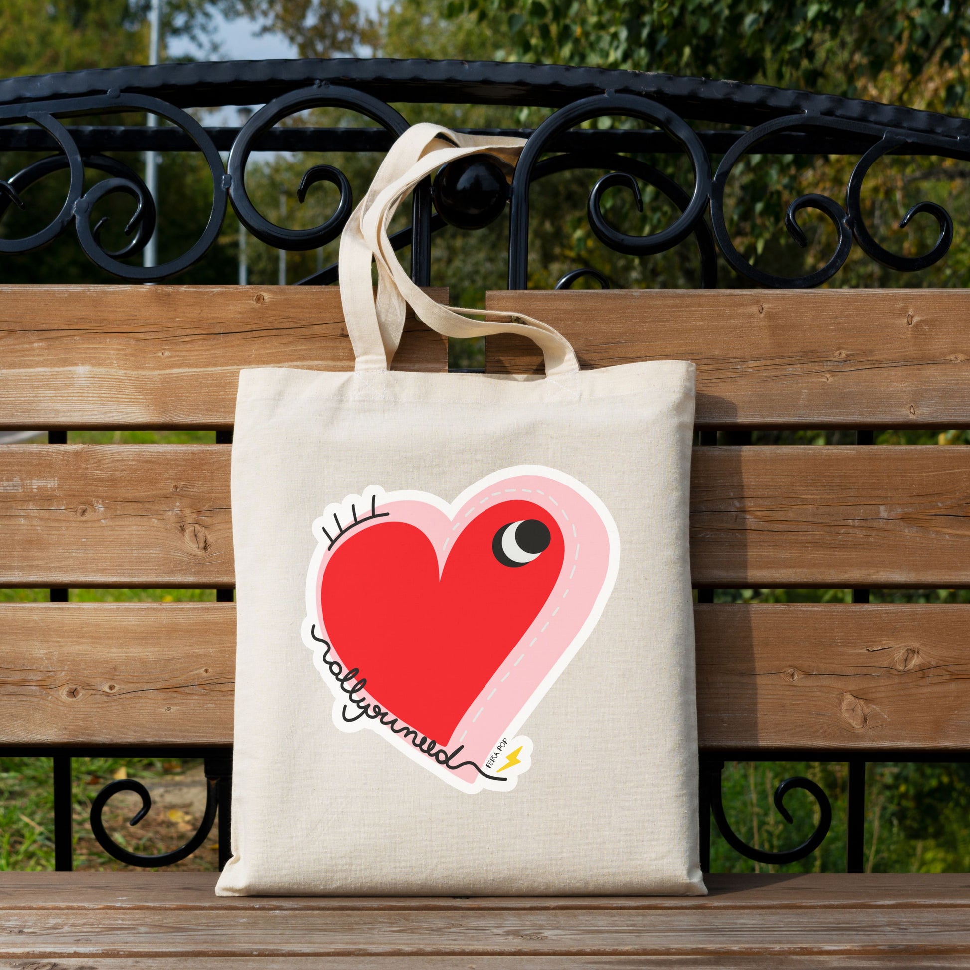All You Need Tote Bag with original drawing of a big red heart with one eye and the words All You Need in playful font, perfect for carrying daily essentials and adding a touch of fun to any outfit.