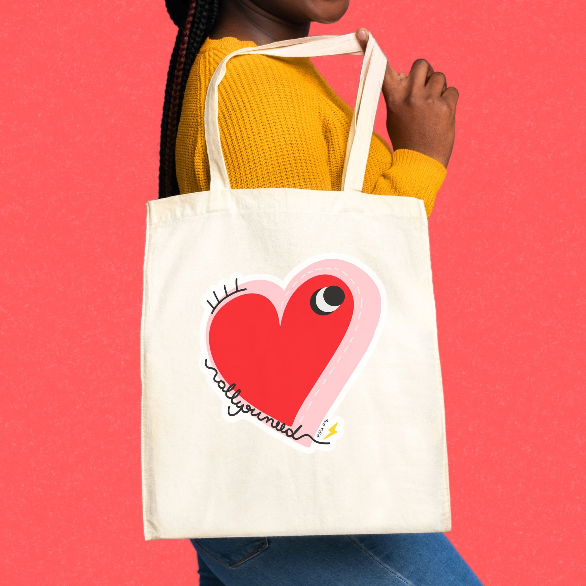 All You Need Tote Bag with original drawing of a big red heart with one eye and the words All You Need in playful font, perfect for carrying daily essentials and adding a touch of fun to any outfit.