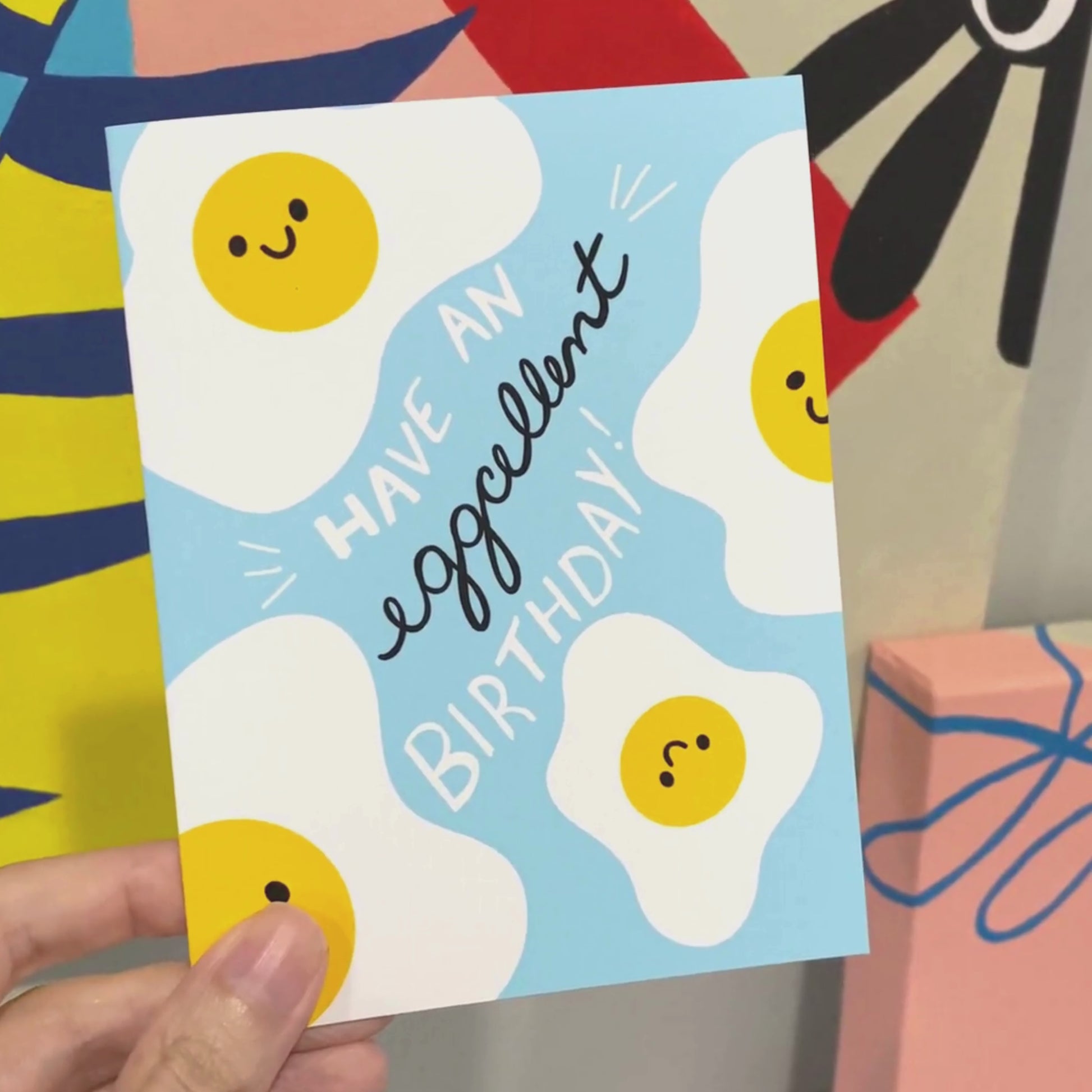Greeting card with the phrase Have An Eggcellent Birthday featuring an original drawing of four sunny-side-up eggs with smiley faces on a light blue background. Perfect for birthday celebrations with a playful and humorous touch.