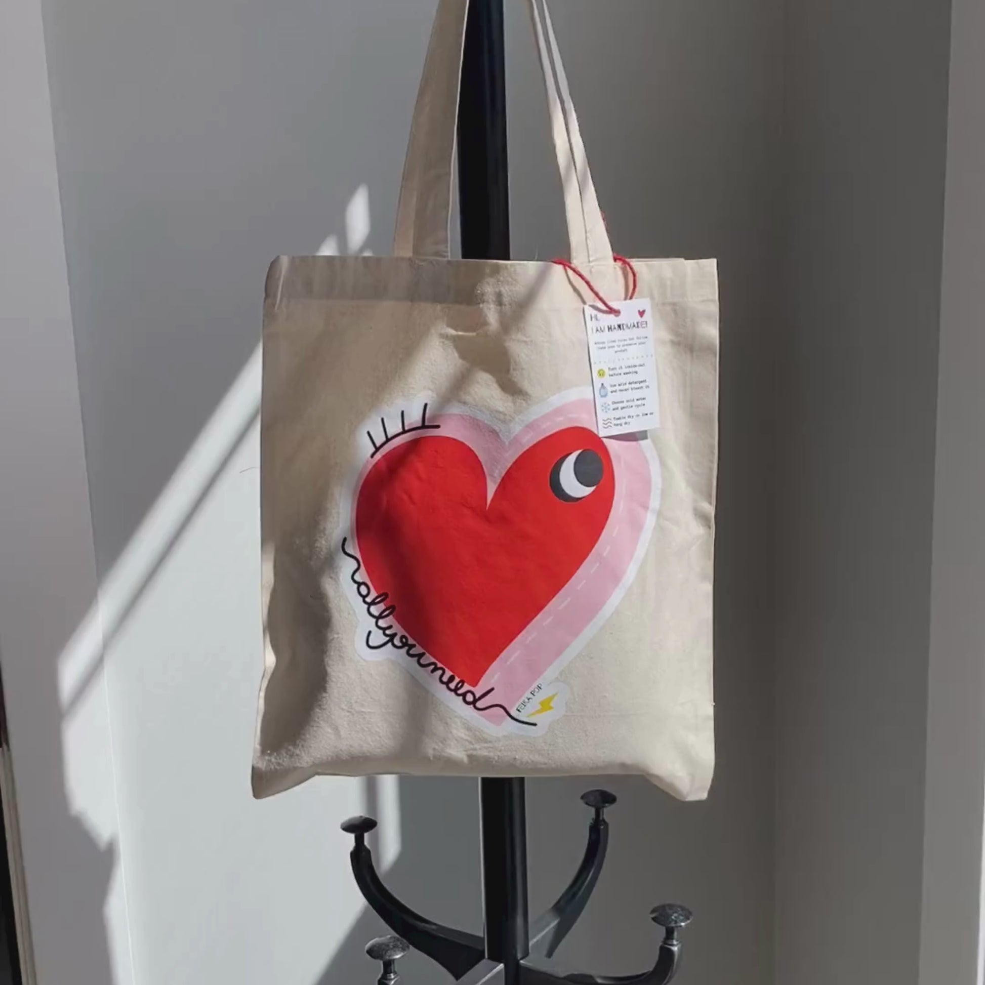 All You Need Tote Bag with original drawing of a big red heart with one eye and the words All You Need in playful font, perfect for carrying daily essentials and adding a touch of fun to any outfit.