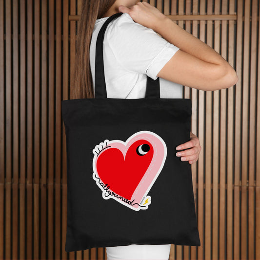 All You Need Tote Bag with original drawing of a big red heart with one eye and the words All You Need in playful font, perfect for carrying daily essentials and adding a touch of fun to any outfit.