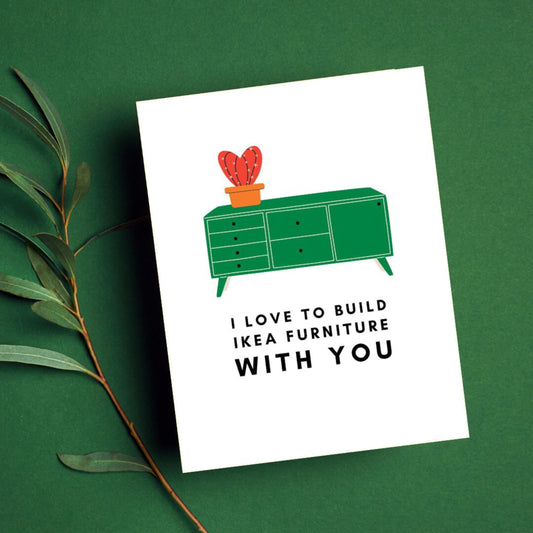 Greeting card with the phrase I Love to Build IKEA Furniture With You featuring a drawing of a green TV stand with a vase holding a red cactus on top. Perfect for celebrating relationships with humor and a nod to DIY adventures.