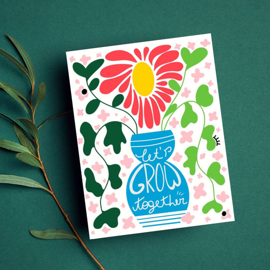 Greeting card with original drawing of blue vase with greenery and big yellow and red flower, phrase Let's Grow Together inside the vase.