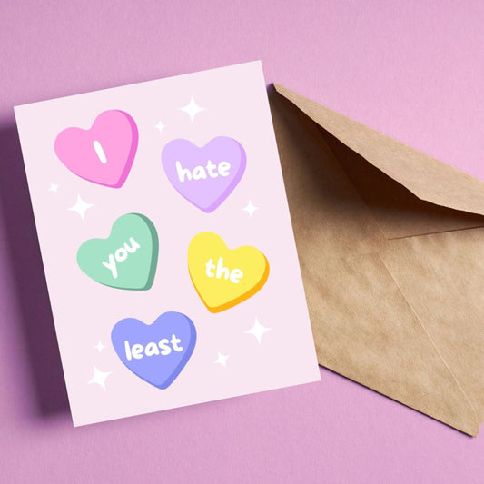 Funny greeting card with conversation heart candies, each displaying a word from the phrase 'I Hate You The Least.' Playful and humorous design perfect for Valentine's Day, friendships, or lighthearted occasions.