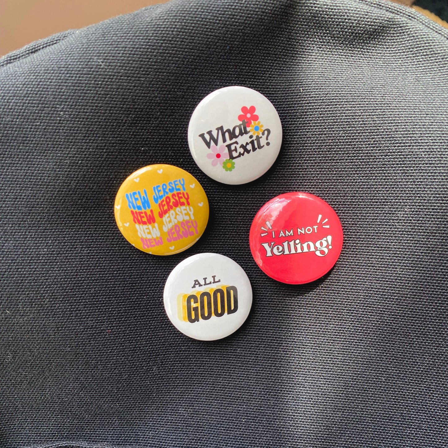 Pack of 4 New Jersey-themed pin-back buttons featuring fun phrases: 'New Jersey,' 'What Exit?,' 'I Am Not Yelling,' and 'All Good.' Perfect for showing Jersey pride with humor and style. Great for New Jersey locals and fans.