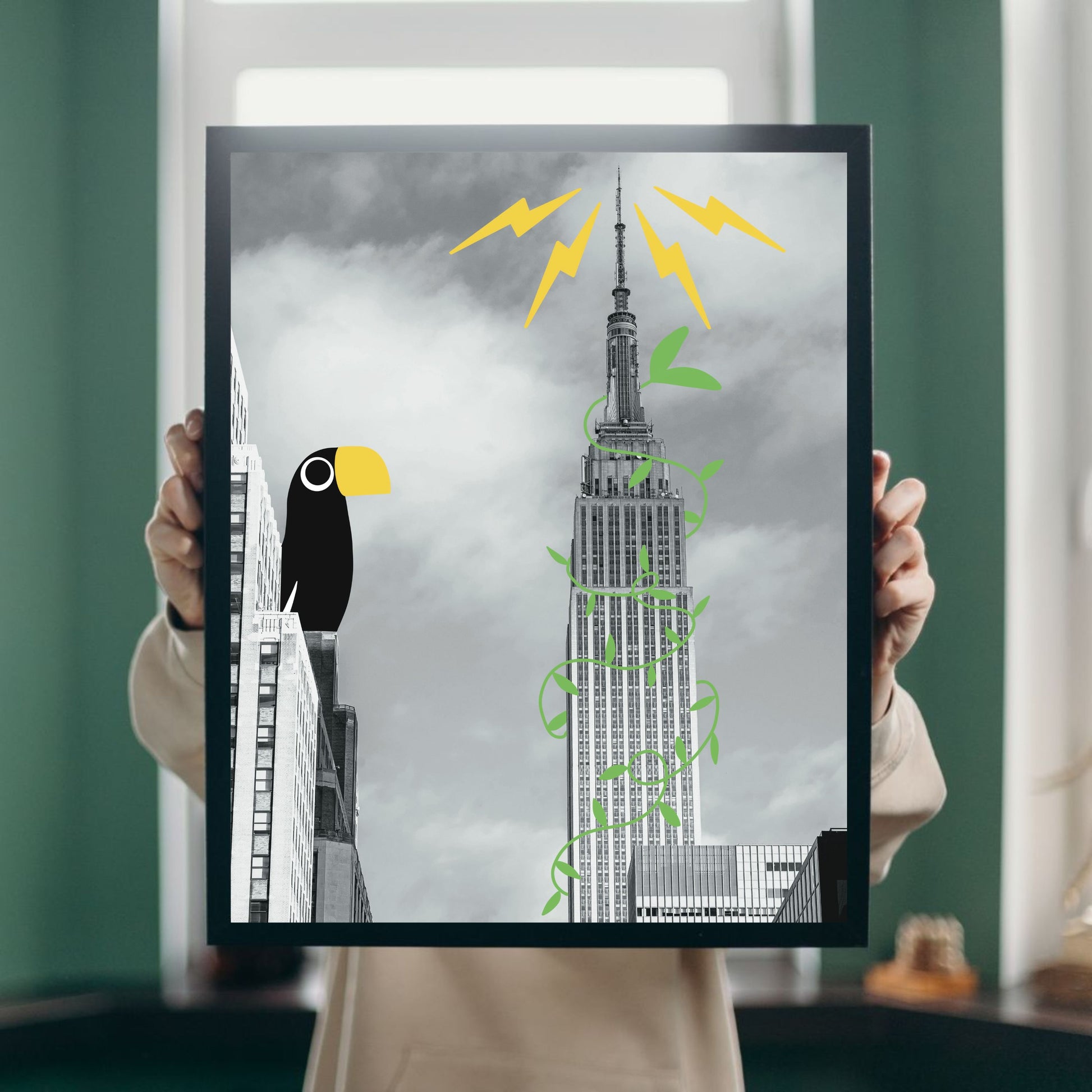 Black and white art print of the Empire State Building with illustrated tropical vines and a colorful toucan perched on a nearby building. Fun surreal wall art titled “Tropical Empire,” perfect for city lovers and modern home decor.
