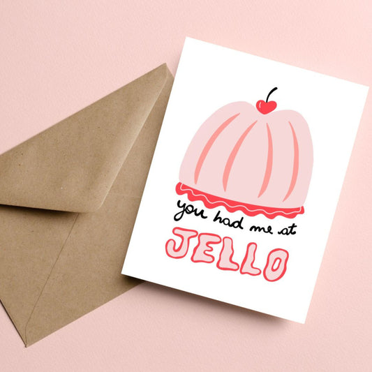 Greeting card with the phrase You Had Me At Jello featuring an original drawing of a pink gelatin dessert with a heart-shaped cherry on top. Perfect for expressing affection with humor and charm.