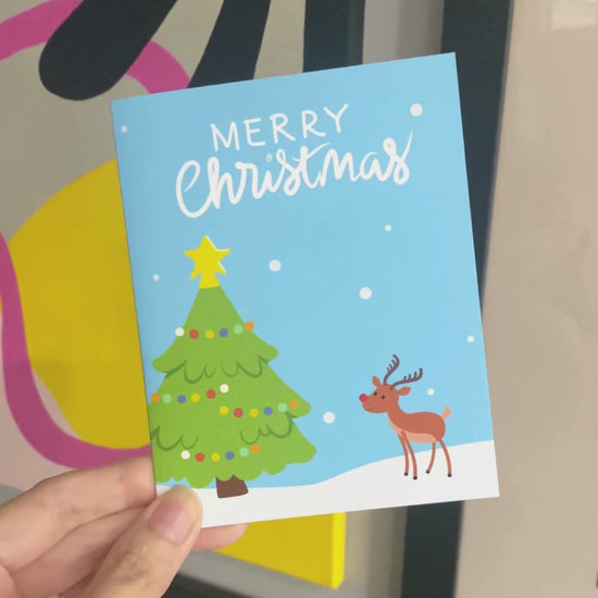 Christmas greeting card with a snowy landscape, decorated Christmas tree, and a cute red-Nosed Reindeer, featuring the phrase 'Merry Christmas' in bold letters, perfect for spreading festive cheer and holiday wishes.